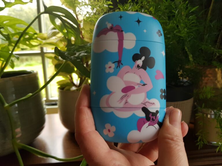 Picture of a hand holding a sky blue Fussy Deodorant case with pictures representing period poverty
