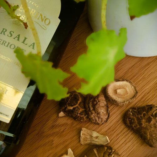 Bottle of Marsala Wine with dried shiitake and mixed mushrooms scattered beneath a plant