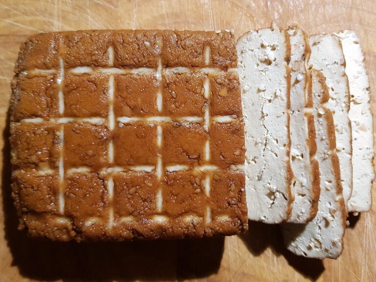 block of smoked tofu on a wooden chopping board, marked with grid lines to simplify cutting