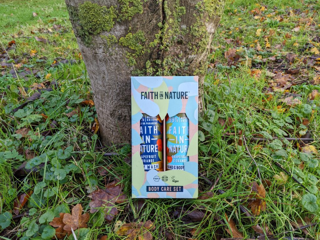 Boxed Faith in Nature Grapefruit and Orange Body Care set sitting on the grass at the bottom of a tree.