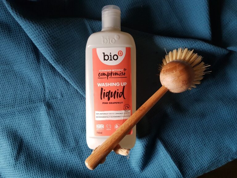 Bottle of Bio D washing up liquid with a bamboo washing up brush on a mid blue background