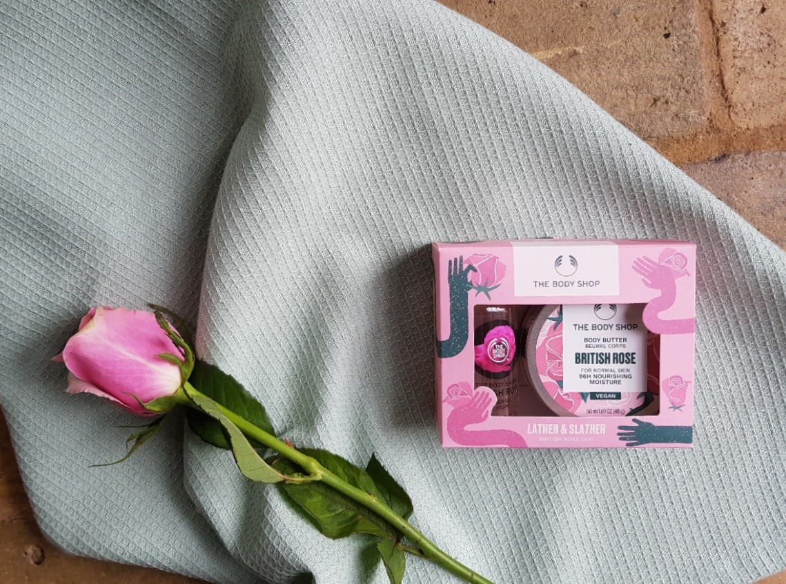Pink gift box containing Body Shop Rose shower gel and body butter, lying on a soft green background next to a pink rose