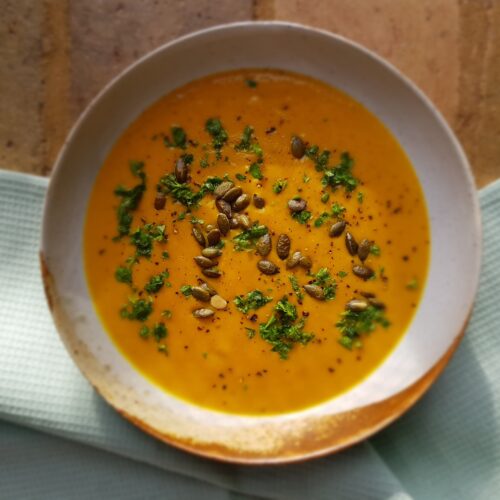 Bowl of orange carrot and cumin soup with parsley and toasted pumpkin seeds