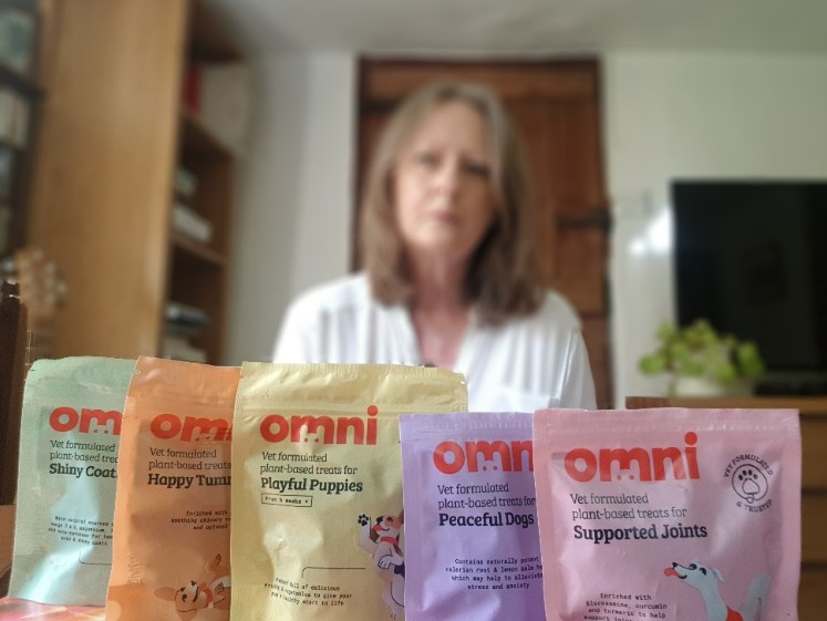 blurred picture of the website owner, vegan mum, in the background, with 5 packs of Omni vegan dog treats displayed in front of her