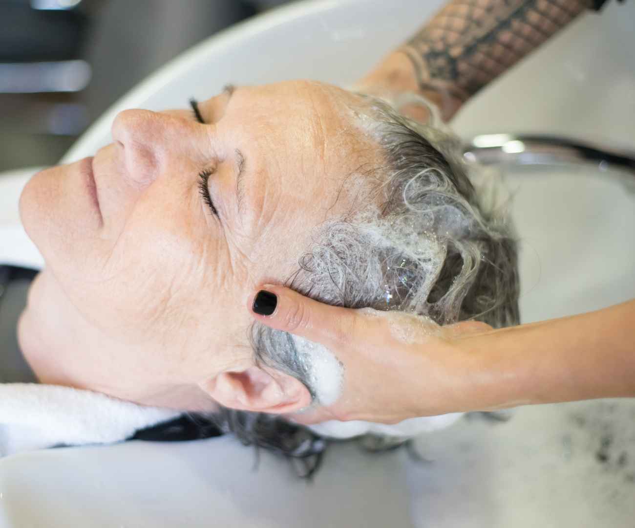 image of female having her grey hair washed at a hairdresser's basin to illustrate this guide to vegan shampoo and conditioner brands