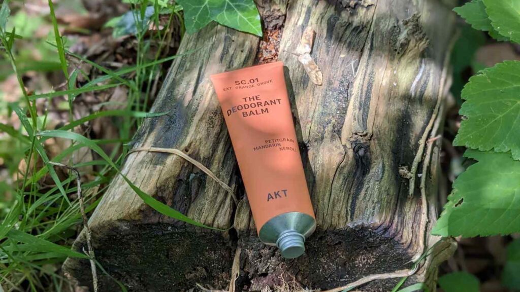 Orange tube of AKT natural deodorant balm lying on a log in dappled sunlight