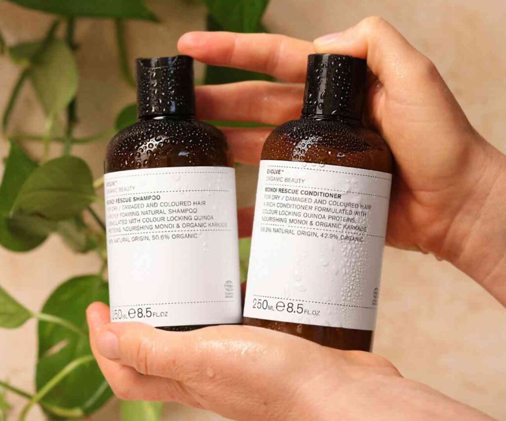 2 hands holding bottles of Evolve Beauty's Monoi vegan shampoo and conditioner