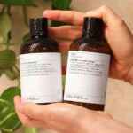 2 hands holding bottles of Evolve Beauty's Monoi vegan shampoo and conditioner