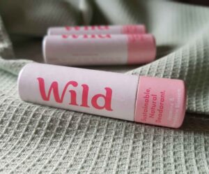 3 small pink and white cylindrical cardboard tubes, close up. Branded with the Wild deodorant logo and containing a travel-sized sample of the deodorant. All the tubes are lying side-on on a green waffled material