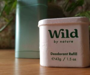 Wild deodorant compostable refill in front of a pale metallic green Wild deodorant refillable case